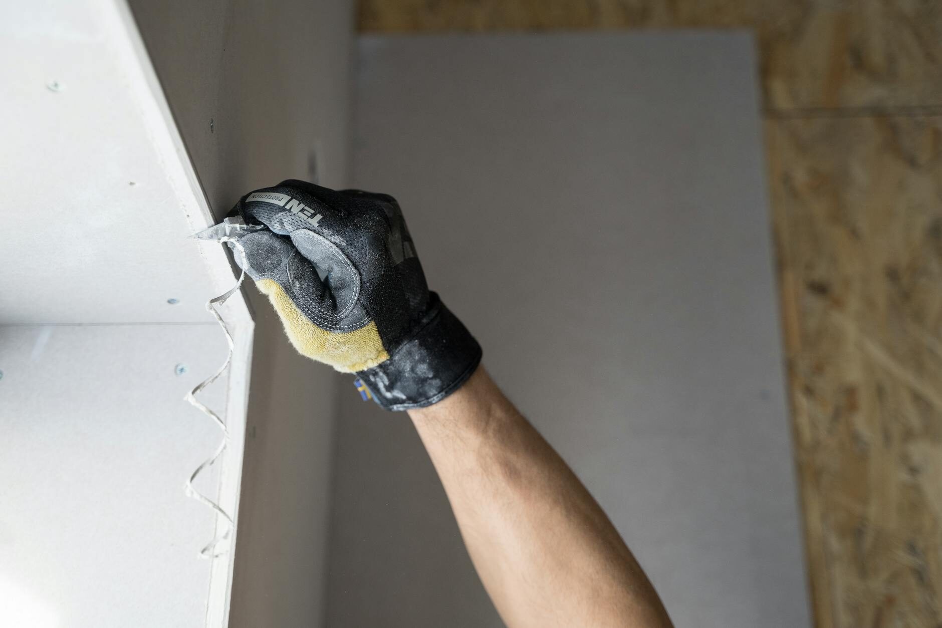 Gloved hands smoothing drywall tape at a wall corner