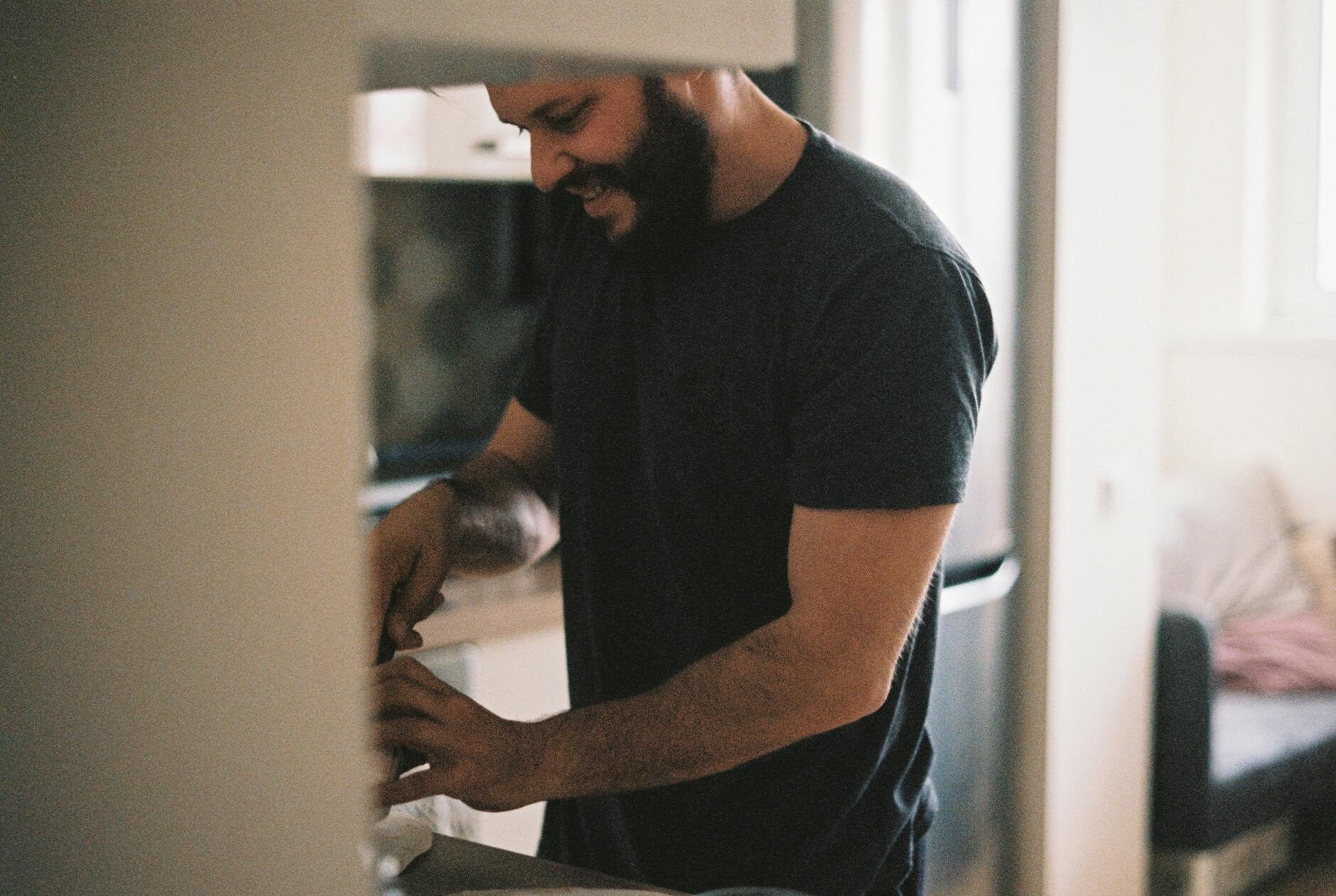 Bearded man smiling while working at a kitchen counter in warm natural light