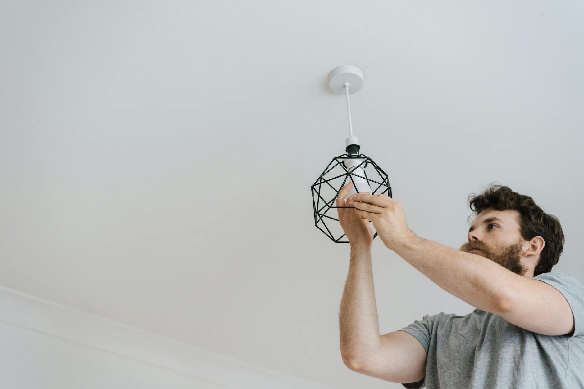 Man reaching up to install a geometric light fixture on a white ceiling