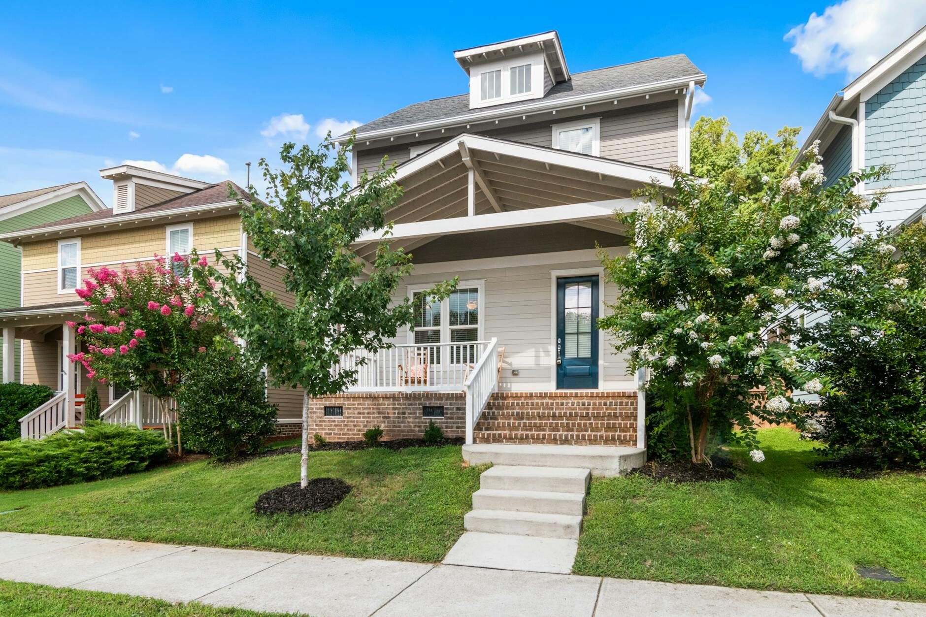 White craftsman bungalow with crepe myrtle trees and a front porch on a sunny day