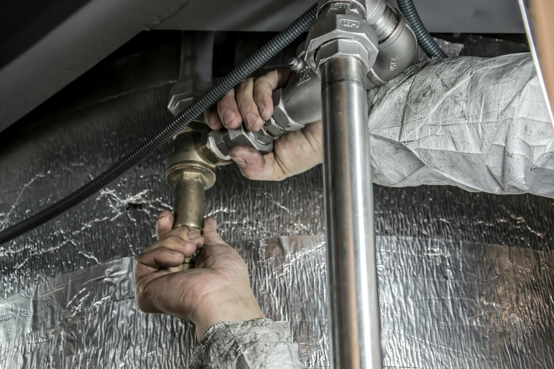Plumber's hands installing pipe fittings under a kitchen sink