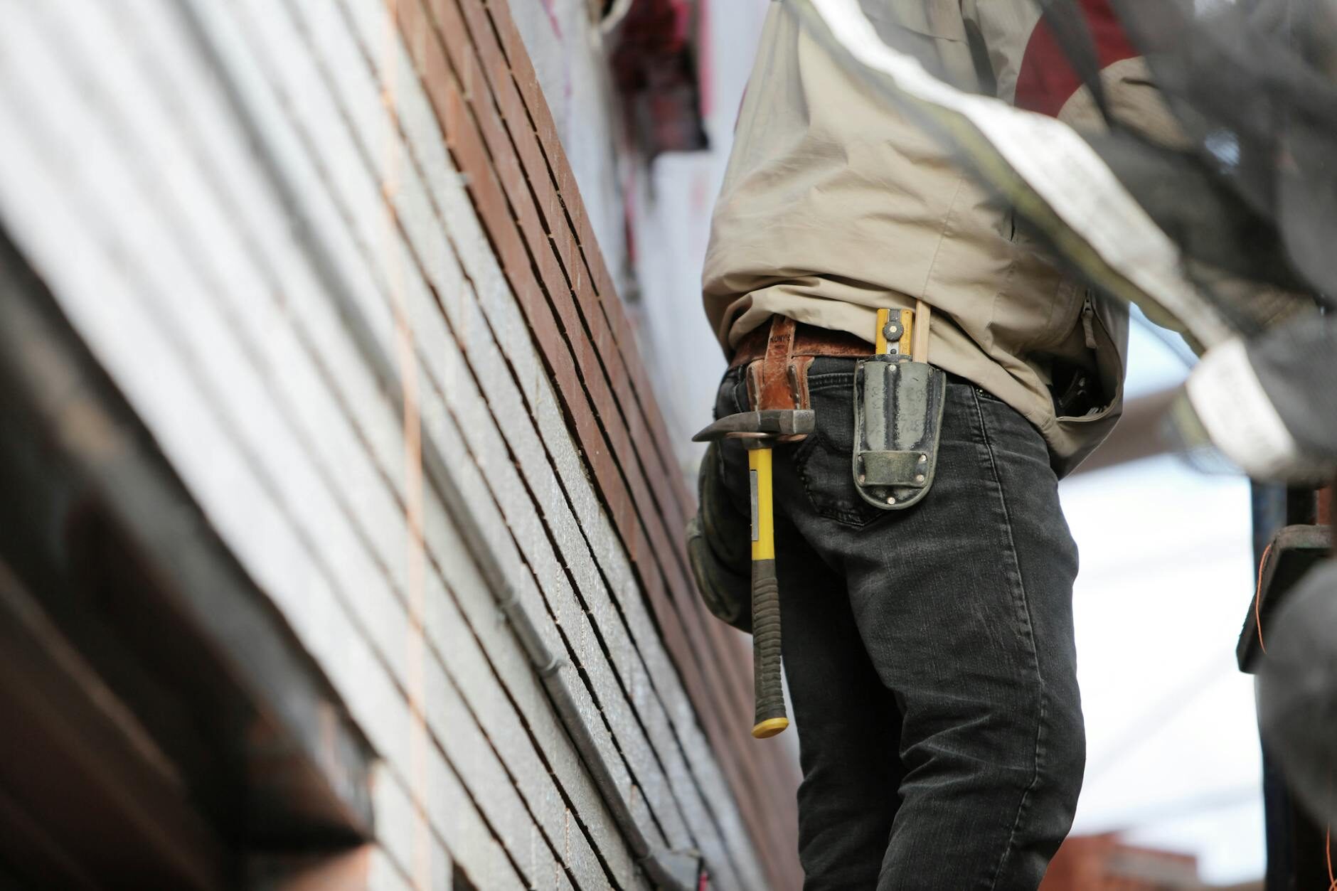 Person from behind wearing a leather tool belt with hammer near wood siding